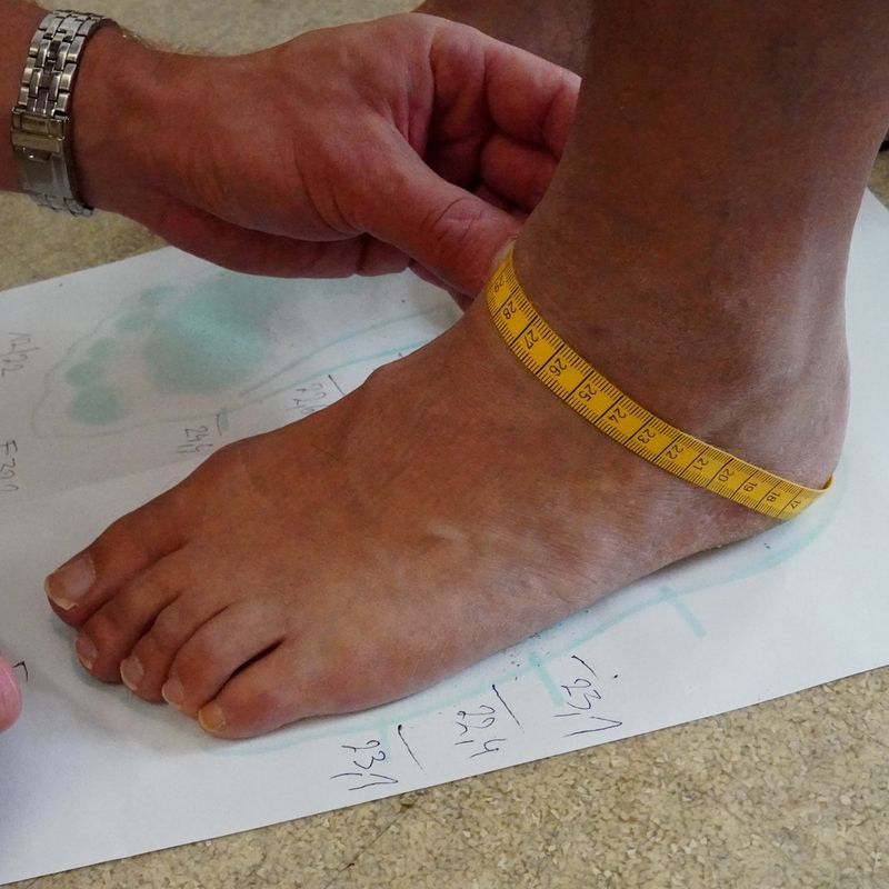 Ein Mann misst einen Fuß mithilfe eines Maßbands ab.