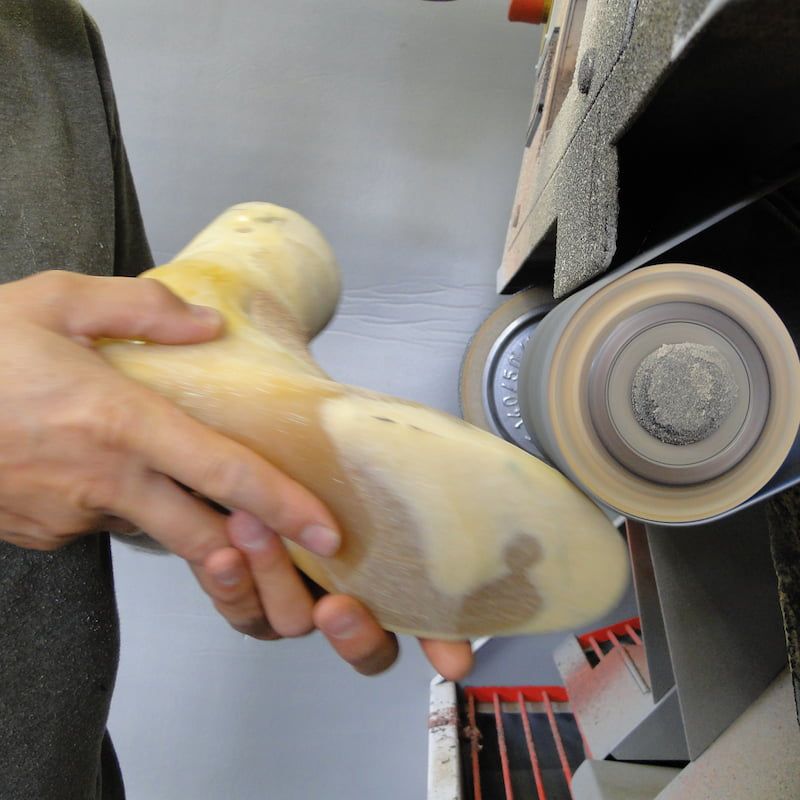 Orthopädieschuhmacher bei der Feinbearbeitung eines individuellen Schuhleistens an einer Schleifmaschine.