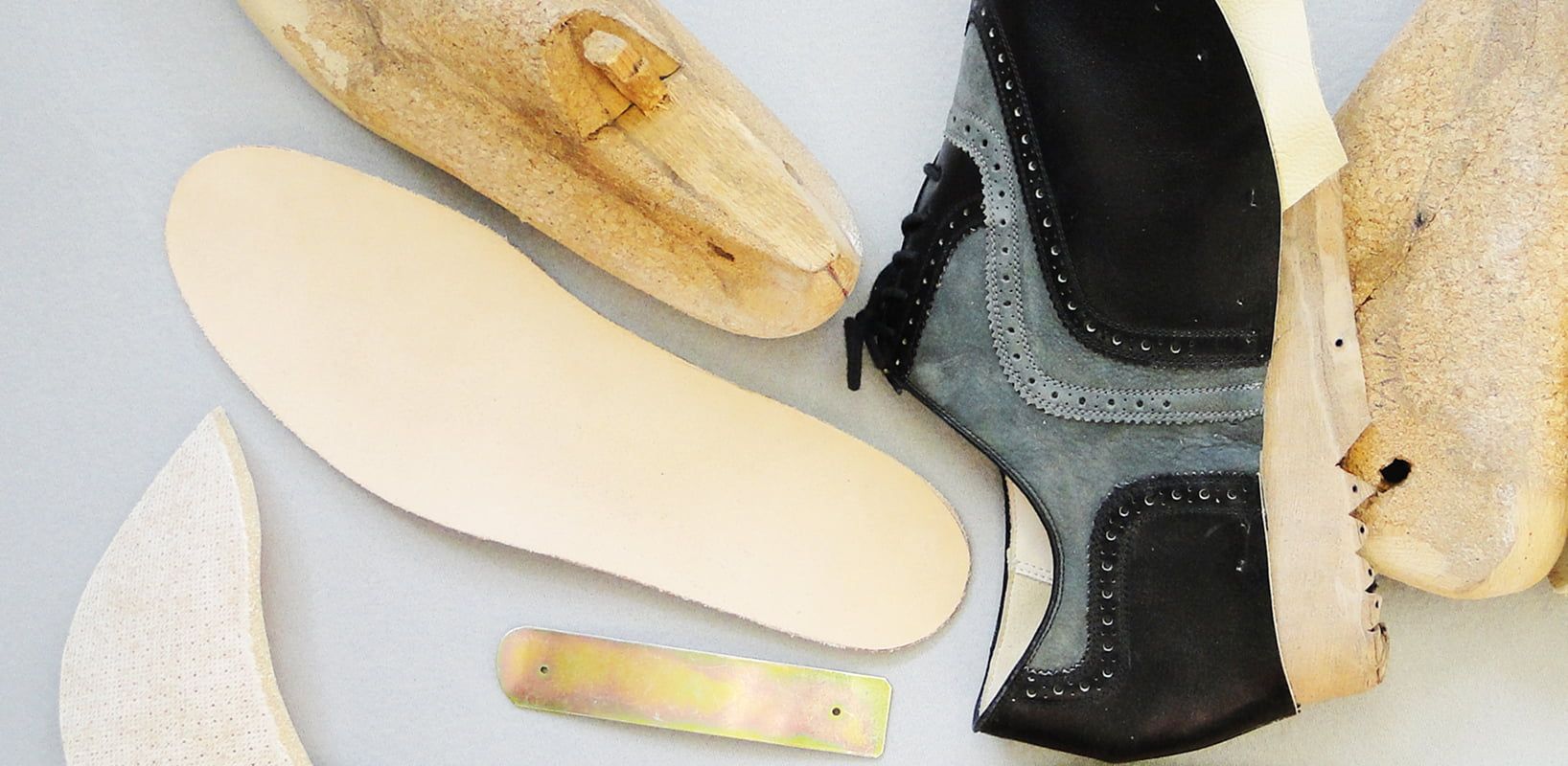 Schuhleisten aus Holz sowie Lederteile, Sohle und Werkzeug für die traditionelle Schuhfertigung auf hellem Grund.