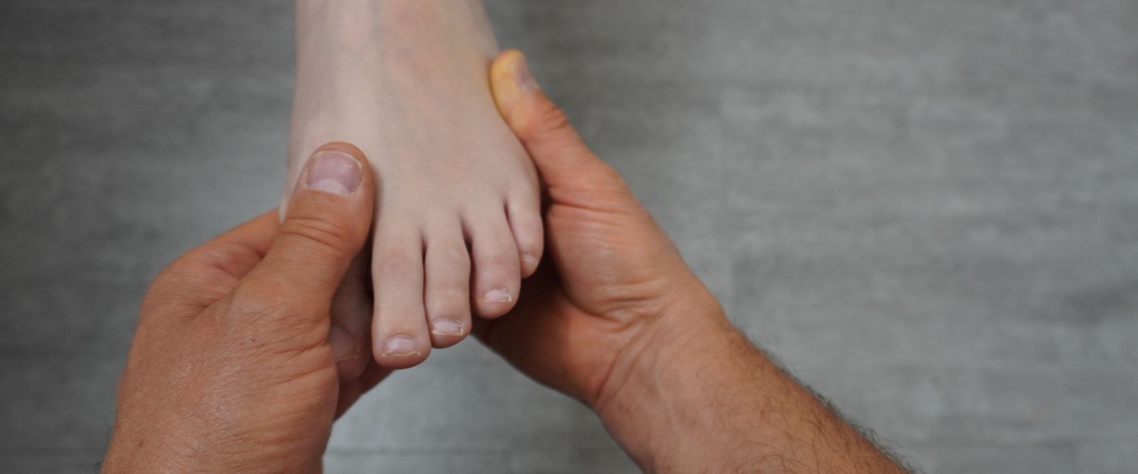 Ein Mann untersucht einen Fuß mit seinen Händen.