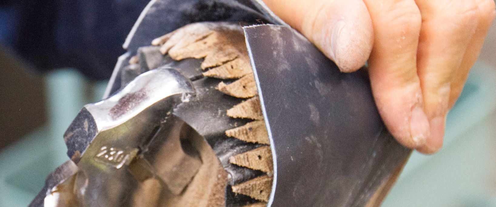 Nahaufnahme: Ein Schuhmacher bearbeitet mit einem Hammer das über einen Leisten gespannte Leder am Schuhboden.